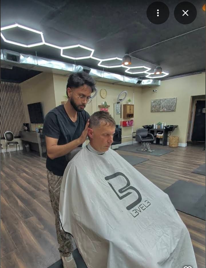 A barber tending to a client's face and beard with a steaming towel at Open Chair