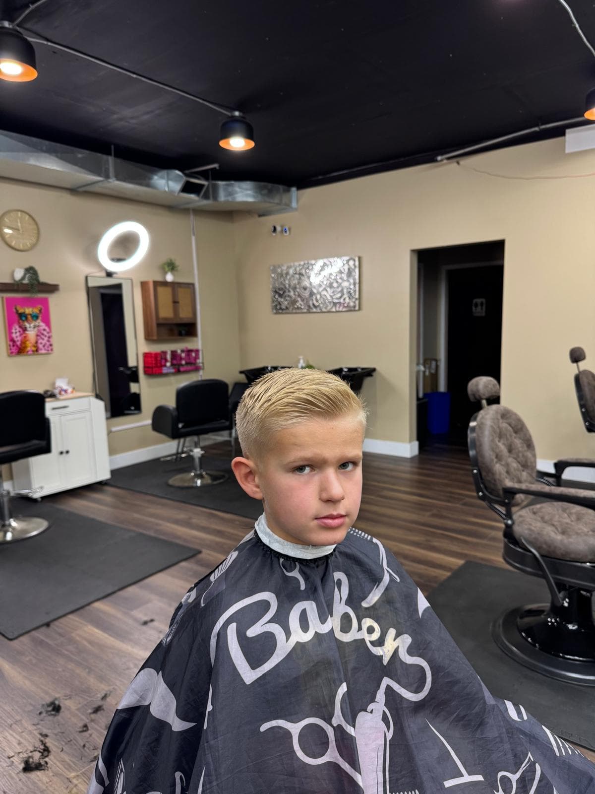 A young boy in a colourful cape, ready for his haircut at Open Chair